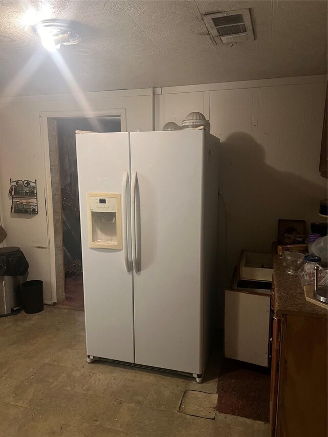 kitchen featuring white cabinets, white fridge with ice dispenser, and a textured ceiling