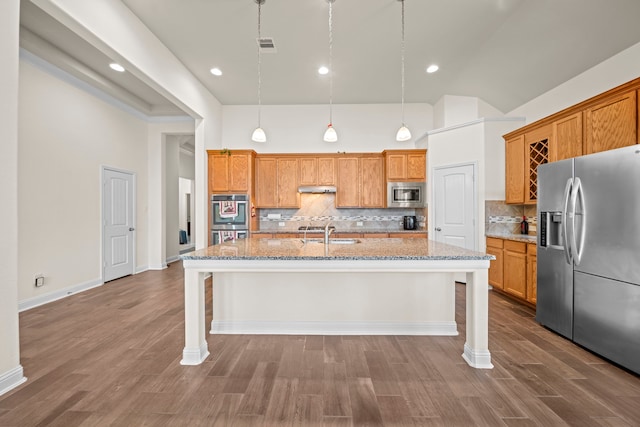 kitchen with stainless steel appliances, hanging light fixtures, a kitchen island with sink, and a kitchen breakfast bar