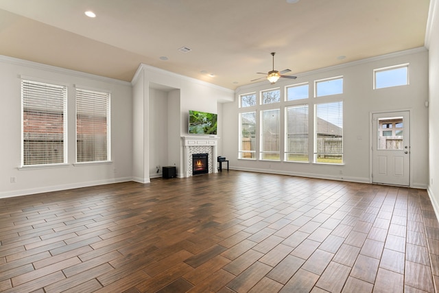 unfurnished living room featuring a tiled fireplace, plenty of natural light, dark wood-type flooring, and ceiling fan