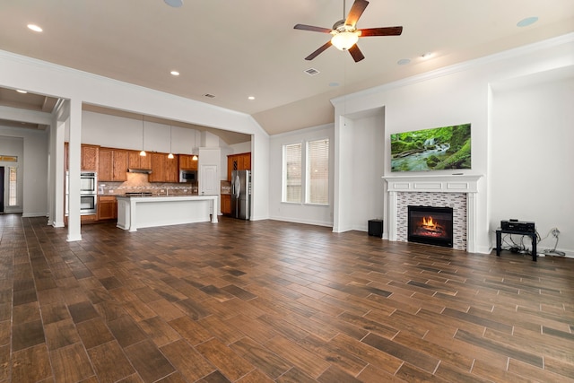 unfurnished living room with baseboards, dark wood finished floors, ceiling fan, a tiled fireplace, and crown molding