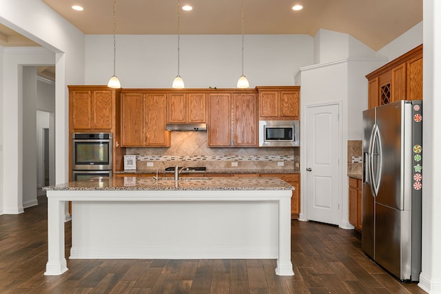 kitchen featuring brown cabinetry, light stone counters, stainless steel appliances, and under cabinet range hood