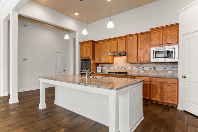 kitchen with under cabinet range hood, brown cabinets, and appliances with stainless steel finishes