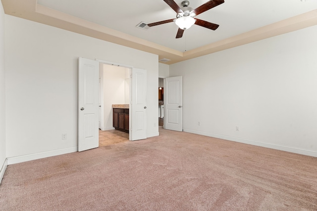 unfurnished bedroom with visible vents, connected bathroom, baseboards, light colored carpet, and a raised ceiling