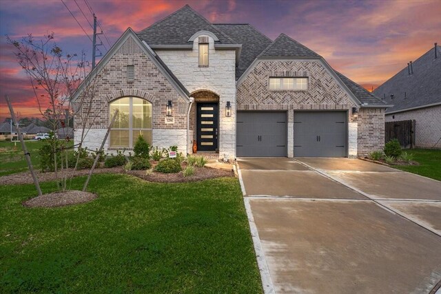 french country inspired facade featuring driveway, brick siding, roof with shingles, and a front yard