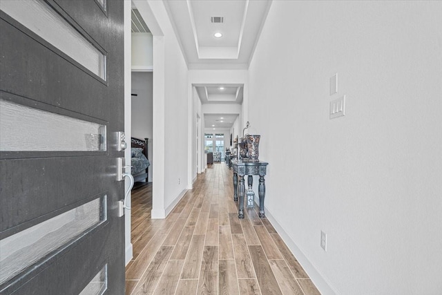 corridor with wood-type flooring and a tray ceiling