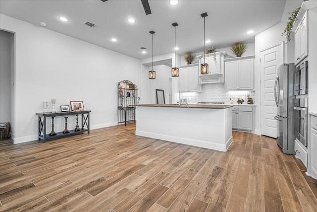 kitchen with decorative light fixtures, visible vents, an island with sink, and white cabinetry