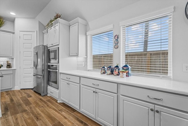 kitchen featuring dark wood finished floors, stainless steel appliances, light countertops, backsplash, and white cabinetry