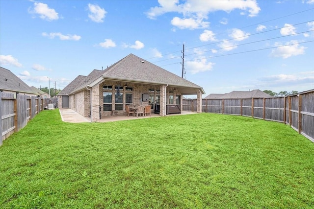 rear view of house featuring a yard, brick siding, a patio area, and a fenced backyard