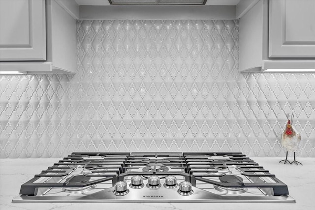 room details with light stone countertops, stainless steel gas stovetop, white cabinetry, and backsplash