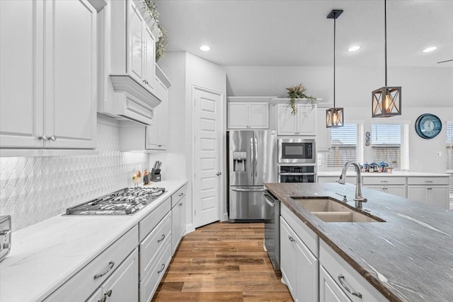 kitchen with decorative light fixtures, stainless steel appliances, white cabinetry, a sink, and wood finished floors