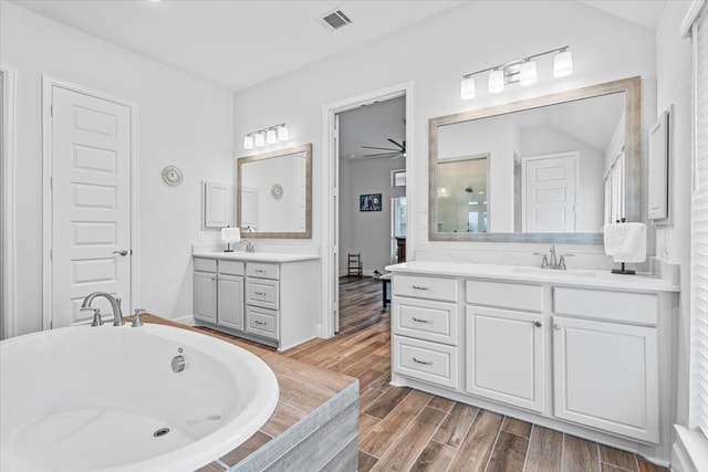 bathroom featuring visible vents, a sink, wood tiled floor, a bathtub, and two vanities