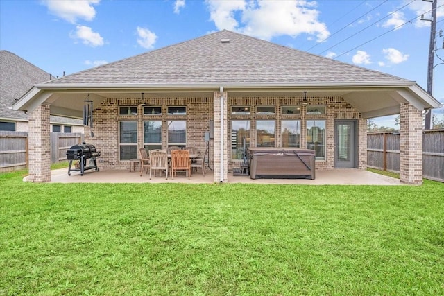 back of house with roof with shingles, brick siding, a hot tub, a patio area, and a fenced backyard