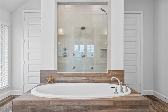 bathroom with a stall shower, baseboards, a bath, and wood finished floors