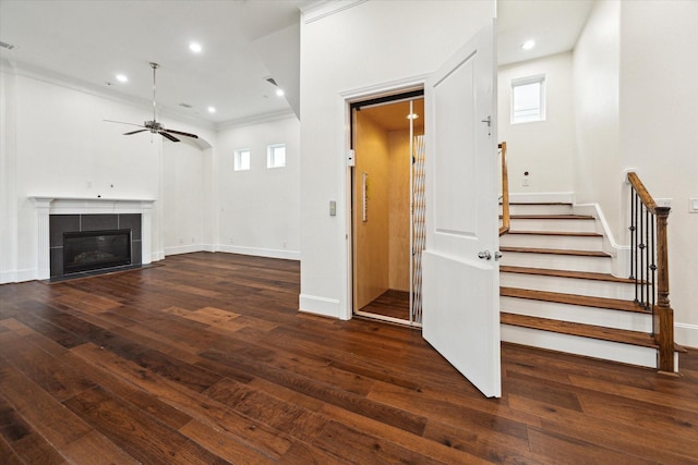 unfurnished living room with dark hardwood / wood-style floors, ceiling fan, crown molding, and a tiled fireplace