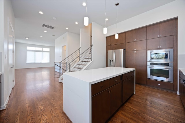 kitchen with appliances with stainless steel finishes, dark brown cabinetry, pendant lighting, dark hardwood / wood-style floors, and a kitchen island