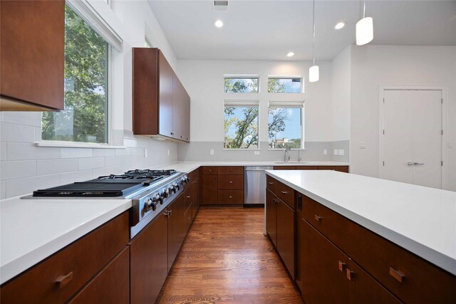 kitchen featuring appliances with stainless steel finishes, dark hardwood / wood-style flooring, backsplash, sink, and decorative light fixtures