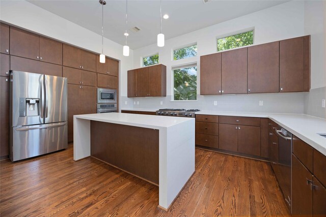 kitchen with dark brown cabinetry, dark wood-type flooring, tasteful backsplash, a kitchen island, and appliances with stainless steel finishes