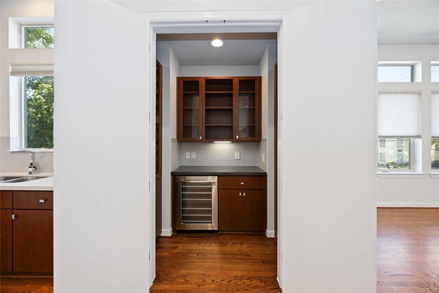 bar with tasteful backsplash, dark brown cabinetry, beverage cooler, dark wood-type flooring, and sink