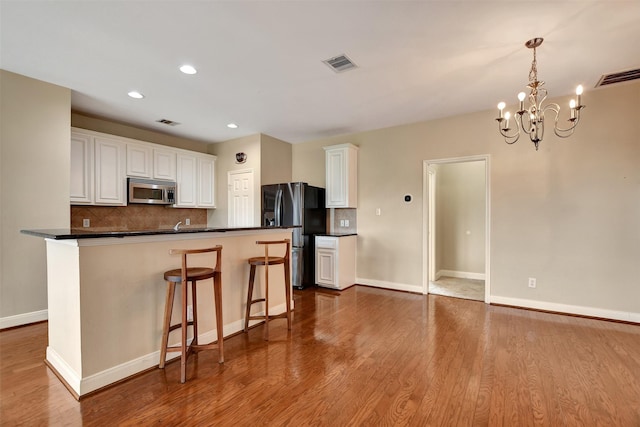 kitchen with white cabinets, a notable chandelier, stainless steel appliances, and light hardwood / wood-style flooring