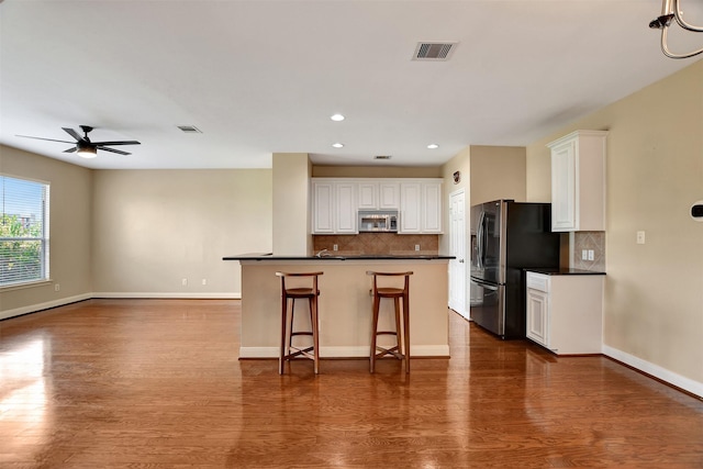 kitchen with a kitchen bar, white cabinets, stainless steel appliances, and hardwood / wood-style flooring