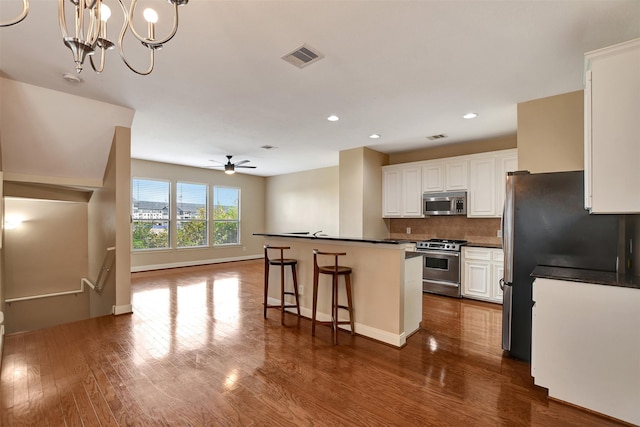 kitchen featuring white cabinets, stainless steel appliances, hanging light fixtures, and dark wood-type flooring