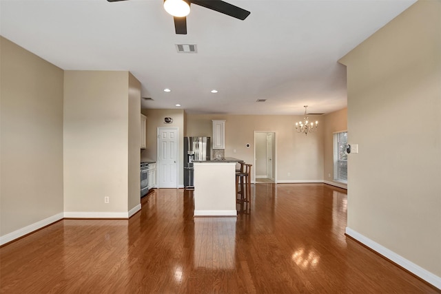 unfurnished living room featuring ceiling fan with notable chandelier and dark wood-type flooring