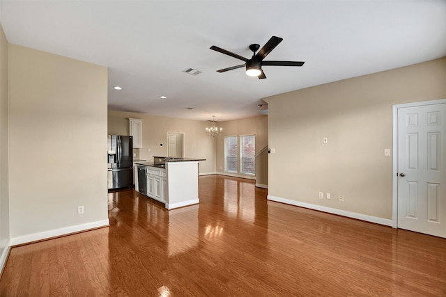 interior space featuring black refrigerator with ice dispenser, ceiling fan with notable chandelier, light hardwood / wood-style flooring, a kitchen island, and white cabinetry