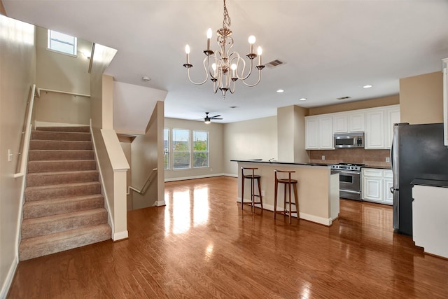 kitchen featuring ceiling fan with notable chandelier, hardwood / wood-style flooring, appliances with stainless steel finishes, a kitchen bar, and white cabinetry