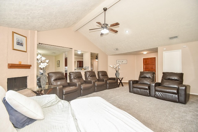 carpeted home theater room with ceiling fan, lofted ceiling with beams, a large fireplace, and a textured ceiling