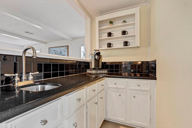 kitchen with tasteful backsplash, white cabinetry, beamed ceiling, sink, and dark stone counters