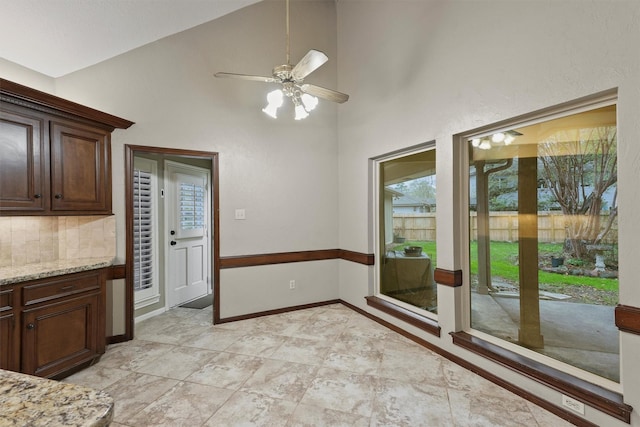 unfurnished dining area with baseboards, high vaulted ceiling, and a ceiling fan