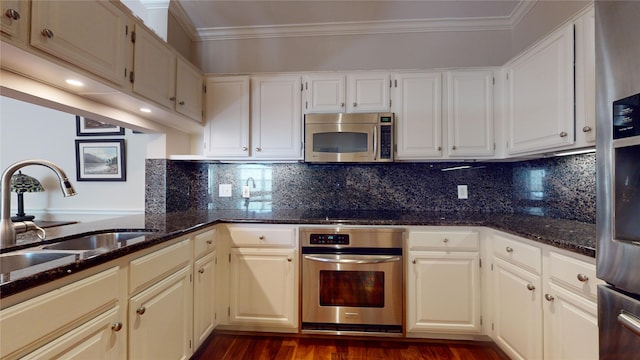 kitchen featuring appliances with stainless steel finishes, ornamental molding, dark stone counters, sink, and white cabinetry