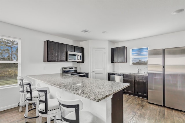 kitchen featuring sink, a breakfast bar area, stainless steel appliances, dark hardwood / wood-style floors, and light stone countertops