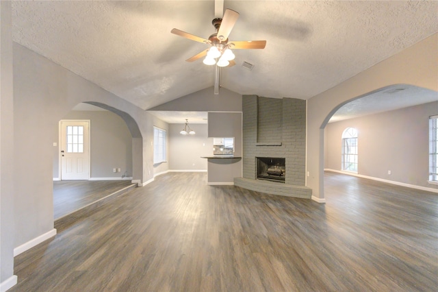 unfurnished living room featuring ceiling fan, a brick fireplace, lofted ceiling with beams, a textured ceiling, and dark hardwood / wood-style flooring