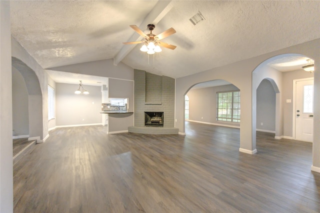 unfurnished living room with ceiling fan with notable chandelier, a textured ceiling, dark wood-type flooring, vaulted ceiling with beams, and a fireplace