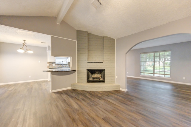 unfurnished living room featuring a textured ceiling, dark wood-type flooring, a fireplace, lofted ceiling with beams, and a chandelier