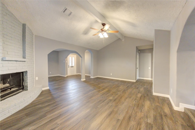 unfurnished living room with ceiling fan, a brick fireplace, dark hardwood / wood-style floors, vaulted ceiling with beams, and a textured ceiling