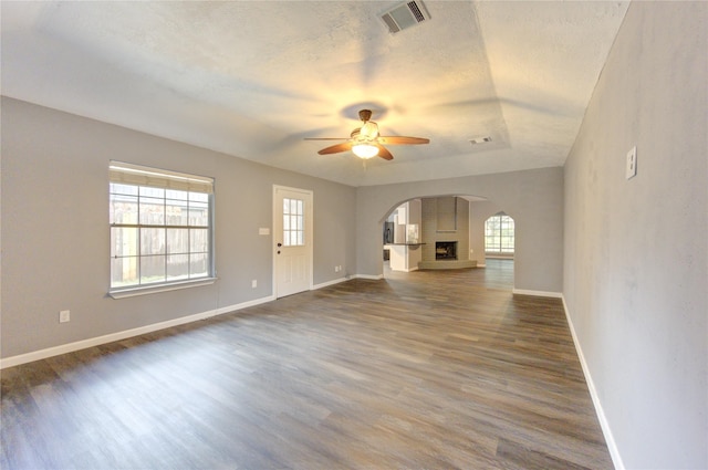 unfurnished living room featuring dark wood-type flooring, ceiling fan, a healthy amount of sunlight, and a textured ceiling