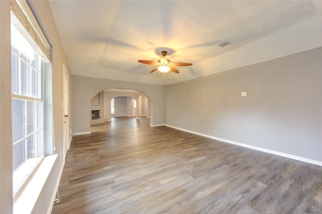 empty room with ceiling fan, wood-type flooring, a wealth of natural light, and a tray ceiling