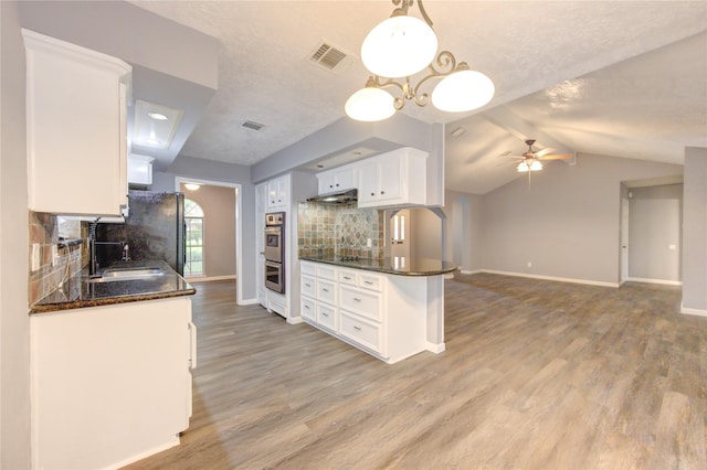 kitchen featuring backsplash, decorative light fixtures, vaulted ceiling with beams, white cabinets, and sink