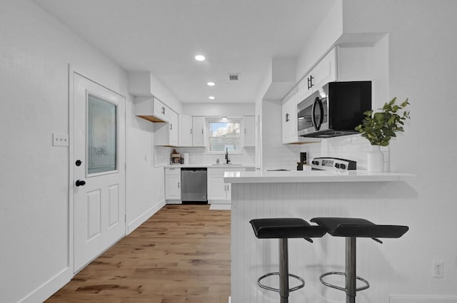 kitchen with kitchen peninsula, stainless steel appliances, sink, light hardwood / wood-style flooring, and white cabinetry