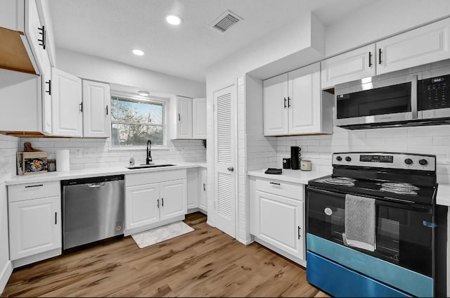 kitchen with appliances with stainless steel finishes, light hardwood / wood-style floors, white cabinetry, and sink