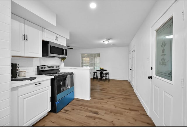 kitchen with kitchen peninsula, decorative backsplash, light hardwood / wood-style flooring, black electric range, and white cabinetry