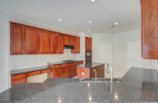 kitchen with decorative backsplash, dark stone counters, a kitchen island with sink, black appliances, and sink