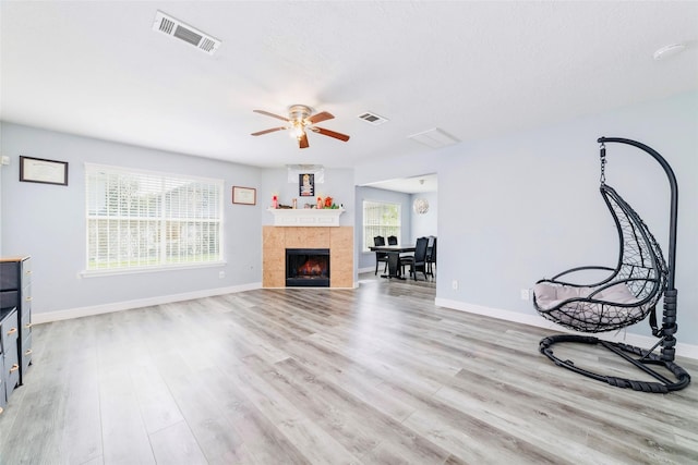 unfurnished living room with a tile fireplace, a wealth of natural light, light wood-type flooring, and ceiling fan