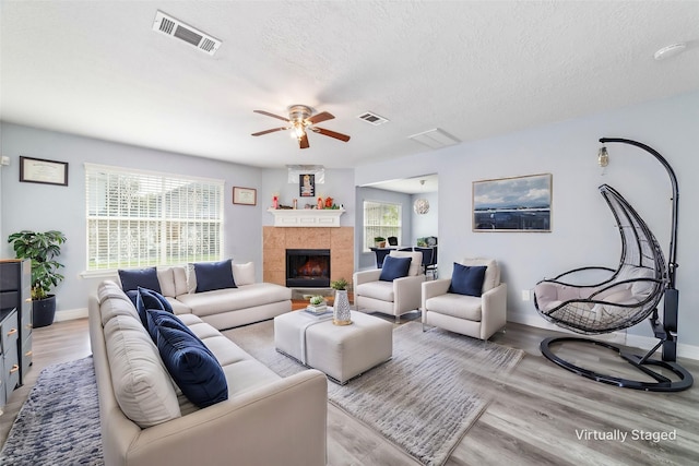 living room featuring ceiling fan, a fireplace, light hardwood / wood-style floors, and a textured ceiling