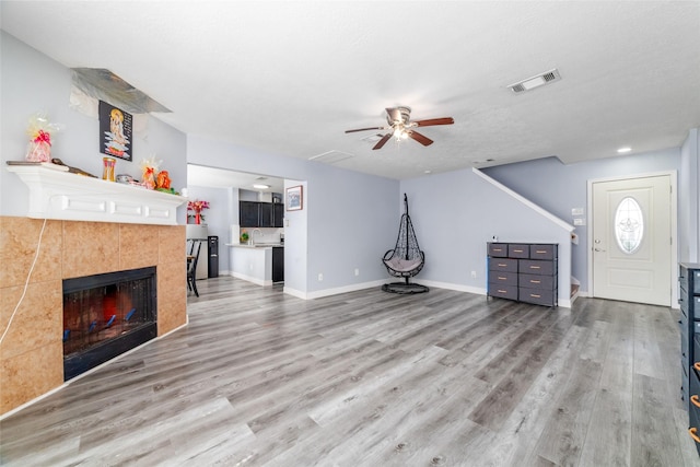 unfurnished living room featuring hardwood / wood-style flooring, ceiling fan, a textured ceiling, and a tile fireplace