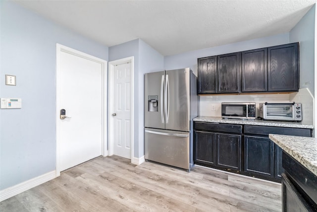 kitchen featuring a textured ceiling, light stone counters, light wood-type flooring, and stainless steel appliances