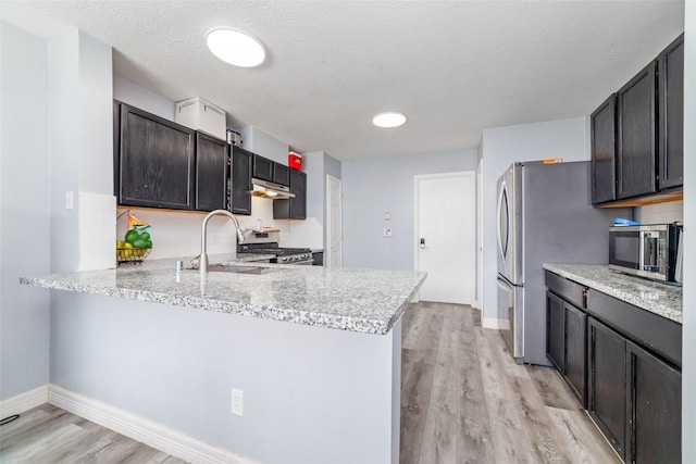 kitchen featuring kitchen peninsula, appliances with stainless steel finishes, light stone countertops, a textured ceiling, and light hardwood / wood-style flooring