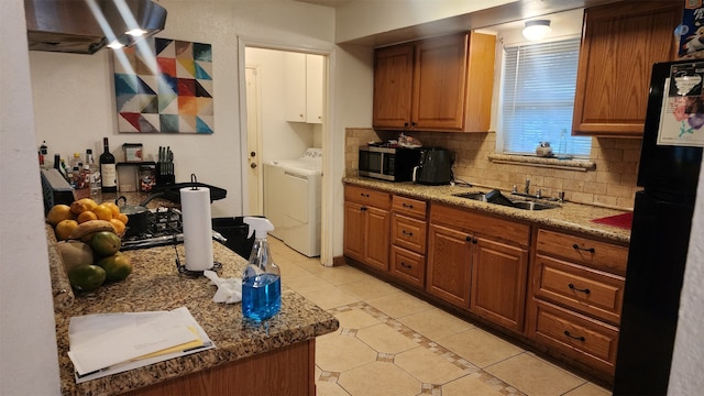 kitchen with washing machine and clothes dryer, sink, black fridge, tasteful backsplash, and dark stone counters